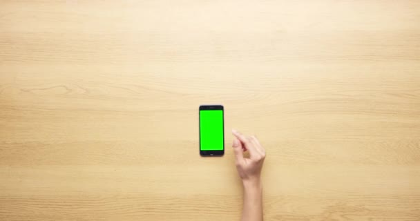 上の木のテーブルの広告かマーケティングのための緑のスクリーンが付いている人 手および電話 モバイルスマートフォンディスプレイ デジタルアプリ またはモックアップスペースでクローズアップするユーザーのトップビュー — ストック動画