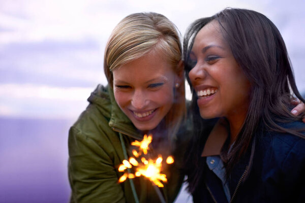 Women, friends and happy with sparklers outdoor, celebration and fun with hiking or travel in nature. Friendship, bonding and sparks with horizon, smile for adventure together and evening sky.