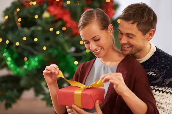 Smile, Christmas gift and couple in living room at home for festive celebration together. Happy, love and young man and woman with holiday present box for xmas event or party at modern house