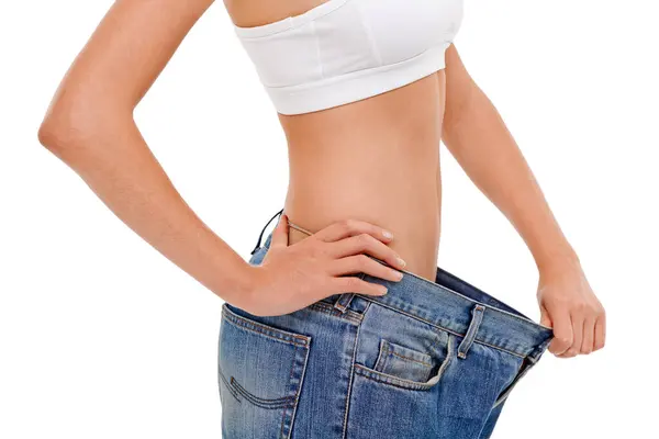 体重減少 フィットネス 運動の結果のためのスタジオで大きなズボンを持つダイエット 白い背景でスリムな胃を測定するためのジーンズ付き女性のウェルネス ボディ クローズアップ — ストック写真