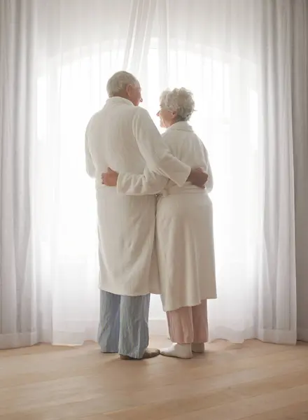 シニアカップル ハグし 休日にパジャマで愛と絆で窓でリラックス ロマンス 朝のルーチンに愛情を抱く高齢者 — ストック写真