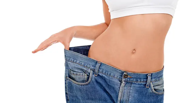 stock image Body, health and woman with big pants in studio for weight loss, fitness or exercise results. Wellness, diet and closeup of female person with jeans for measuring slim stomach by white background