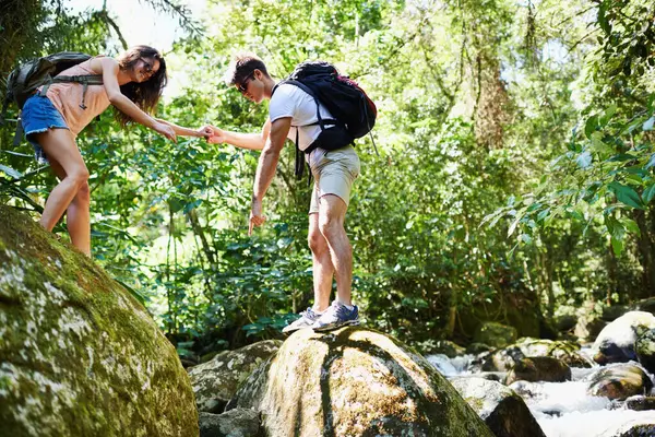 Hiking, help and couple by river in nature for adventure, freedom and explore with backpack outdoors. Forest, travel and man and woman on mountain for holiday, vacation and trekking for wellness.