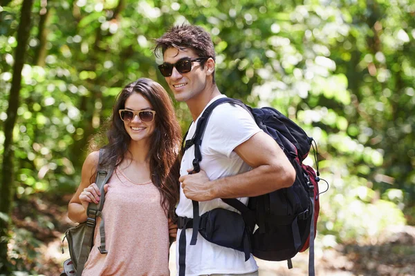 Happy couple, backpack and hiking with sunglasses in nature for adventure or outdoor journey together. Young man, woman or hiker with smile, bag and bonding for trekking or walk in forest or woods.
