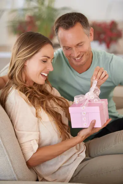 Woman opening gift, man and happiness with surprise for birthday or anniversary, love and support with romance. Couple in marriage, unboxing package with ribbon and present for token of appreciation.