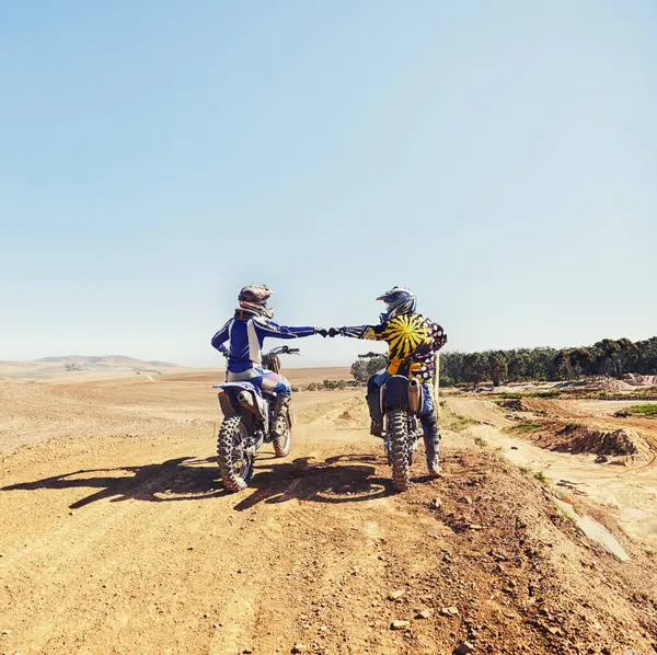 Sport, teamwork or people on motorcycle outdoor on dirt road before racing, challenge or competition on mockup. Motocross, dirtbike driver and fist bump with helmet on offroad course for performance.