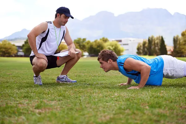 Men, push up and personal trainer on grass for exercise with clipboard for stats, progress or development. Person, coach or mentor with checklist for schedule, training or workout for health on field.