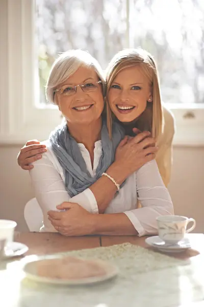 House, hug and girl visit mom for breakfast, coffee and daughter with senior, retirement and embrace. Female person, smile and happiness with mother in family home, elderly and woman in dining room.