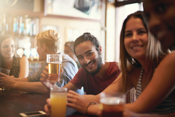 Friends, man and smile in pub with beer for happy hour, relax or social event with confidence. Diversity, people and drinking alcohol in restaurant or club with discussion for bonding and celebration.