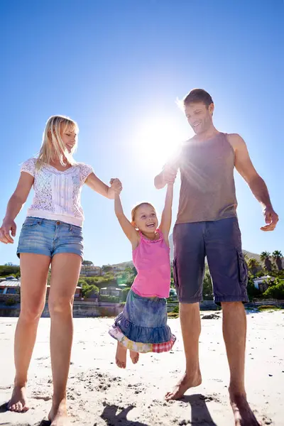 Holding hands, love and happy family at a beach with swing, support and care while bonding in nature. Freedom, travel and kid with parents at the ocean for morning games, fun or adventure at the sea.