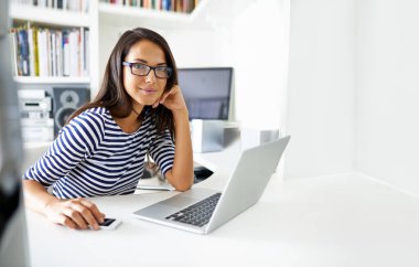 Portre, mutlu öğrenci ve bilgisayar evdeki masada uzaktan öğrenim, öğrenim ya da internetteki uzak eğitim için. Brezilya 'da akıllı telefonlu bilgisayardaki genç kadının yüzü, gözlüğü ve gülümsemesi..