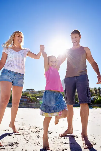 Parents, swing and playing with child at beach in portrait with care, love or bonding in summer on holiday. Father, mother and daughter with games, connection or holding hands in sunshine on vacation.