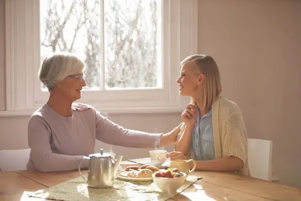 House, woman and daughter visit mom in kitchen with food for breakfast, tea and snacks with senior. Female person, smile and happiness with mother in family home, elderly and girl in dining room.