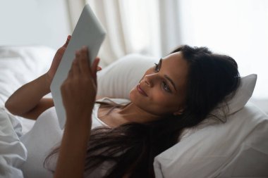 Tablet, yatak ve sosyal medya sabah rahatlamak için, hafta sonları uyanmak ya da kitap okumak için. Çevrimiçi edebiyat veya öykü için yatak odasında genç insanla teknoloji, uygulama ve internet.