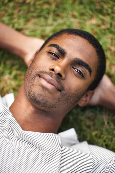 Black man, relax and lying on grass while resting, sleeping and enjoy summer or nature outdoor. Male person, smile and sunshine after holiday, calm guy and happiness in garden or field or outside.