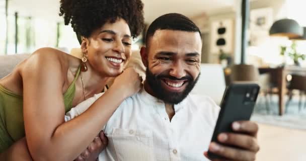 在家里的社交媒体或流媒体订阅的沙发上拥抱 欢笑或快乐的夫妻 手机短信或有趣的人带着微笑 新闻或迷因在网上搜索以放松自己 — 图库视频影像