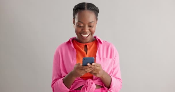 ニュースと興奮する黒人女性 オンライン競争のためのスタジオで携帯電話でグレーの背景に与えます スマートフォンと幸せな女性モデル サインアップのアプリ通知受賞者や賞 — ストック動画