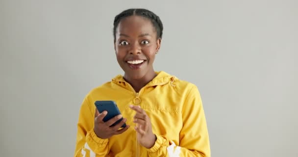スタジオでの携帯電話の勝利のための顔とニュース 賞品のプレゼントの興奮と通知 ブラック女性の人物 オンライン競争の勝利の肖像画とアプリ 宝くじの成功と灰色の背景 — ストック動画