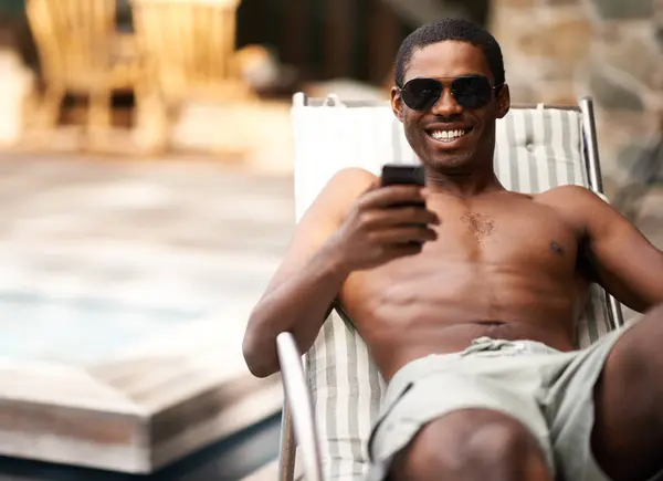 Man, phone and relax on deckchair, happy and scroll on social media on summer holiday. Black male person, weekend and online for blog or app for chat on travel to Nigeria, vacation and outdoors.
