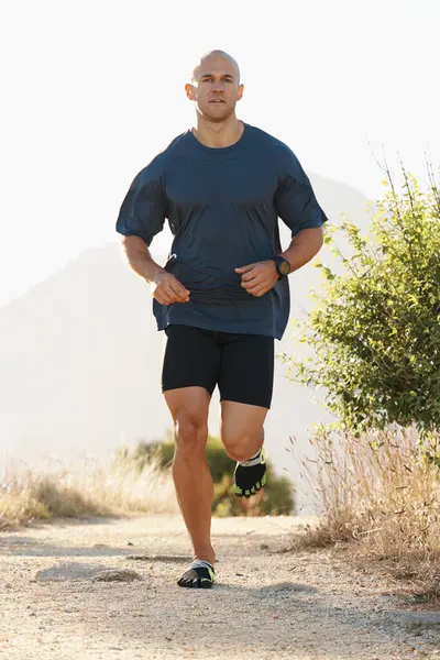Fitness, running and man on path in mountain for health, wellness and strong body development. Workout, exercise and runner on road in nature for marathon training, performance and morning challenge