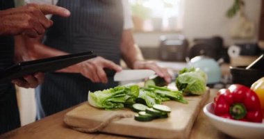 Çift, eller ve evdeki mutfaktaki malzemelerin tarifi veya listesi için tabletle sebze doğrama. Teknolojili insanlara yakın çekim, evde yemek pişirmek için doğal ya da organik gıda.