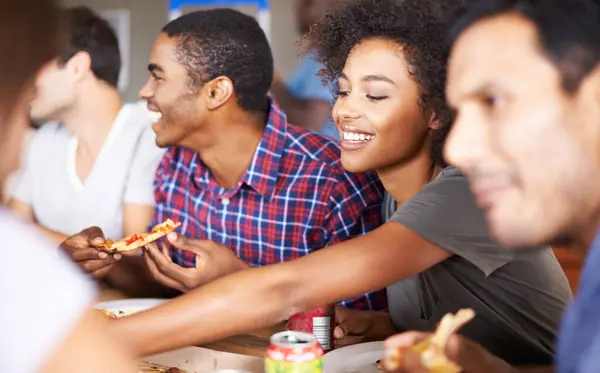 Friends, group and eating of pizza in house with happiness, soda and social gathering for bonding in dining room. Men, women and fast food with smile, drinks and diversity at table in lounge of home.