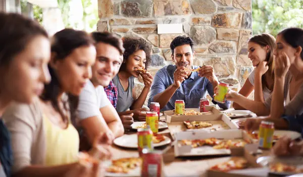 Friends, group and eating of pizza in home with happiness, soda and social gathering for bonding in dining room. Men, women and fast food with smile, drinks and diversity at table in lounge of house.