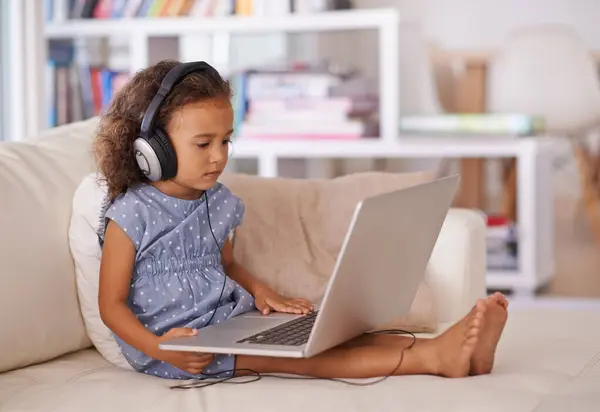 Stock image Kindergarten, elearning and kid on laptop in home with online class, video and girl with headphones. Virtual, education and child with computer on sofa in house for development of language knowledge.