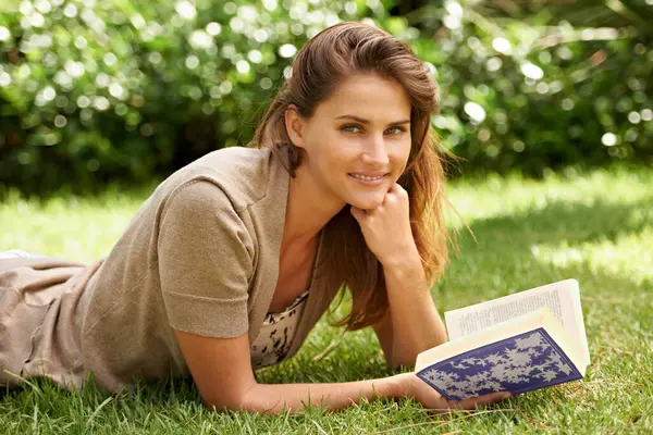 Portrait, book and woman reading on grass, field and nature in garden, backyard and sunshine relax in summer. Female person, gen z girl and novel studying for learning, education and knowledge.