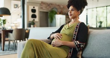 Siyahi kadın, hamile ve kanepesinde bebek için heyecanla, düşüncelerle ve mutlulukla göbek için sevgiyle düşünüyor. Müstakbel anne, karnını ve koltuğunu tut, doğum bakımı hakkında ne düşündüğünü merak et.