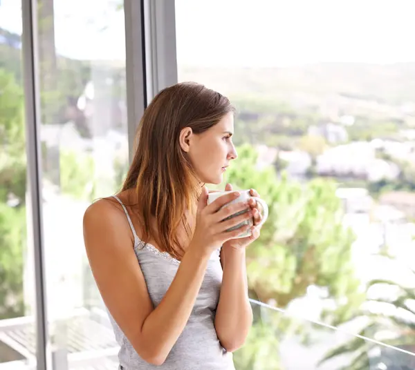 Coffee, woman and relax on balcony with view, weekend and espresso cup for morning inspiration. Young lady, thinking or peace with cocoa for comfort, mindfulness or calm on break in modern apartment.