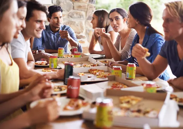 Friends, group and eating of pizza in house with happiness, soda and social gathering for bonding in backyard. Men, women and fast food with smile, drinks and diversity at table in lounge of home.