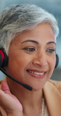 Ofisteki müşteri hizmetleri için çağrı merkezinde kulaklık takan kıdemli kadın, yüz ve danışman. Gülümseyen ve çevrimiçi tavsiye ya da iş yerinde yardım isteyen olgun kadın ya da temsilciye yakın çekim.