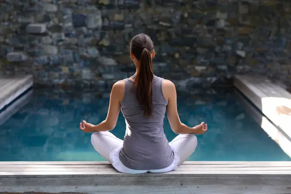 Back, pool and meditation with woman, yoga and fitness with sunshine and peace with breathing. Rear view, person and water with girl and yogi with wellness and healthy with hobby, relax and exercise.