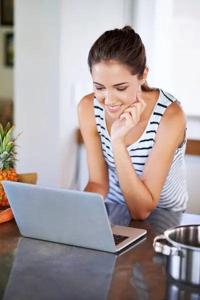 Woman, working and laptop on kitchen counter, happy female person and home on internet. Google it, browsing cooking recipes and social media, online search on technology for healthy food ideas.