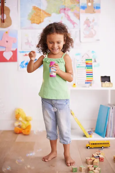 Playing, kid and blowing bubbles with toys for childhood development, smile and having fun alone. Happiness, growth and face of young girl in kindergarten for learning, soap liquid and games.