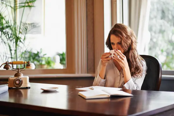Woman, drink and writer with coffee in office to relax before writing on desk, paper or notebook with ideas. Person, thinking and enjoy tea with remote work in home as journalist planning article.