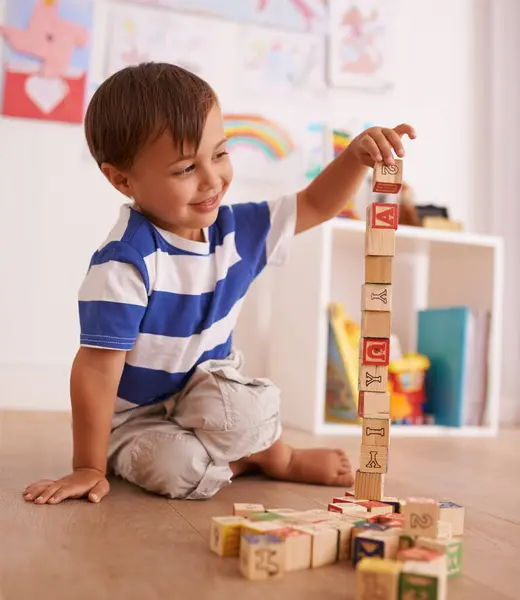 Home, boy or child with building blocks for playing and learning for development or growth in playroom. Happiness, education and playful with activity, young toddler kid and fun games for creativity.
