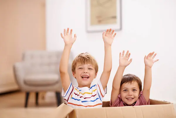 Children, box and play in living room for sibling, child and surprise for hand in air and laugh for joy in home. Young kid, friend and innocent for adorable and cute with boy and carefree for excited.
