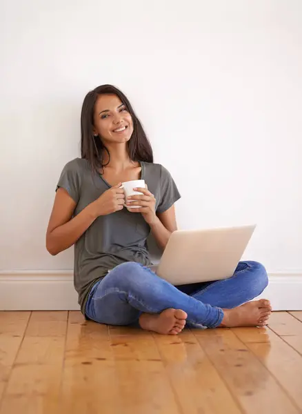 Wall background, laptop and woman with coffee on floor of apartment, home and smile with mug. Happiness, female person and girl watching movies on site of app online with technology and internet.