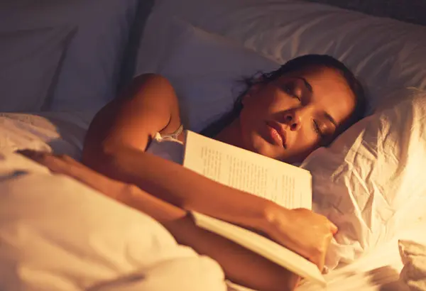 Woman, sleep and book in bed and resting, dreaming female person or night lamp for story and novel. Relax, hobby and tired girl with fantasy or biography, literature or learning for peace in room.
