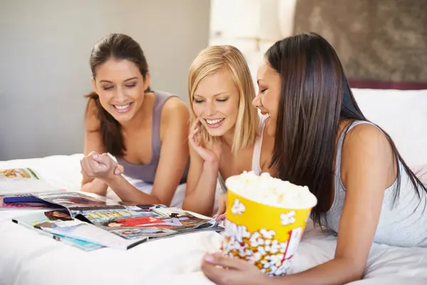Friends, popcorn and reading for sleepover, social and bedroom for bonding and excited group for snacks. Female people, together and magazines for jokes, besties and entertainment with conversation.