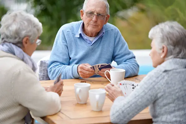 Poker, playing cards and senior group in retirement, outdoor and relaxed in garden, backyard and terrace. Elderly people, bridge and smile with coffee, table and outside for relaxation, fun and games.