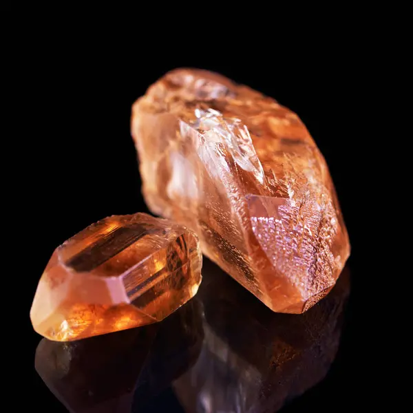 Gem, rock and orange stone in studio with isolated black background for natural resource, shine and sparkle for luxury. Crystal, jewel and reflection in closeup for citrine, glow and mineral.