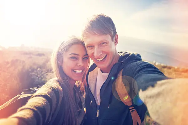 Hiking, selfie and couple hug in nature with love, trust and bonding outdoor together. Backpack, travel or people portrait in countryside for adventure, vacation or romantic profile picture at sunset.