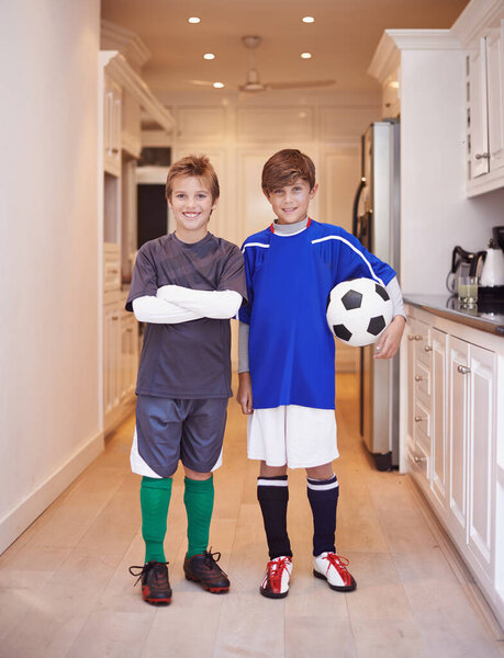 Children, friends and portrait with soccer ball at house or training game in kit or competition, cardio or apartment. Male people, face and football in kitchen or player practice, exercise or workout.