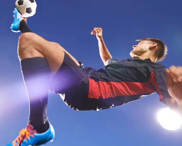 Football player, jump and kick with man and soccer ball, energy and challenge with skill in professional sport. Sky background, light and playing game at arena or stadium, action and exercise outdoor.