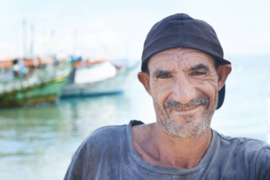 Balıkçı, portre ve gülümseyen haşin bir adam, tekneler ve okyanusta balıkçı teknesi. Kırışıklıklar, Brezilyalı yaşlı ve olgun, mutlu erkek, yakın ve suda göçebe yaşam tarzıyla çalışıyor..