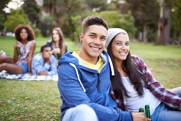 Couple, smile and portrait with beer in park with bonding and fun on campus outdoor. Students, grass and happy together in a university garden on a break on a picnic with college people with drinks.