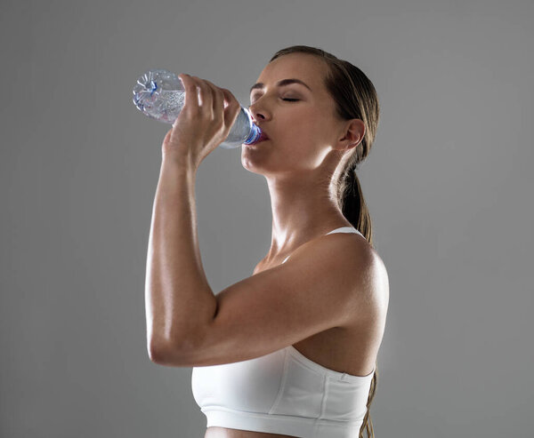 Woman, fitness and drinking with water for hydration after workout or exercise on a gray studio background. Thirsty female person or athlete with bottle of liquid for natural sustainability on mockup.